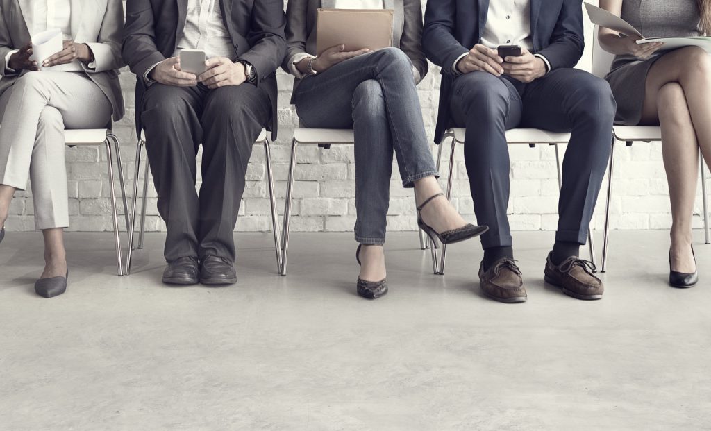 Job candidates waiting for interview with resumes and laptops in hiring office.